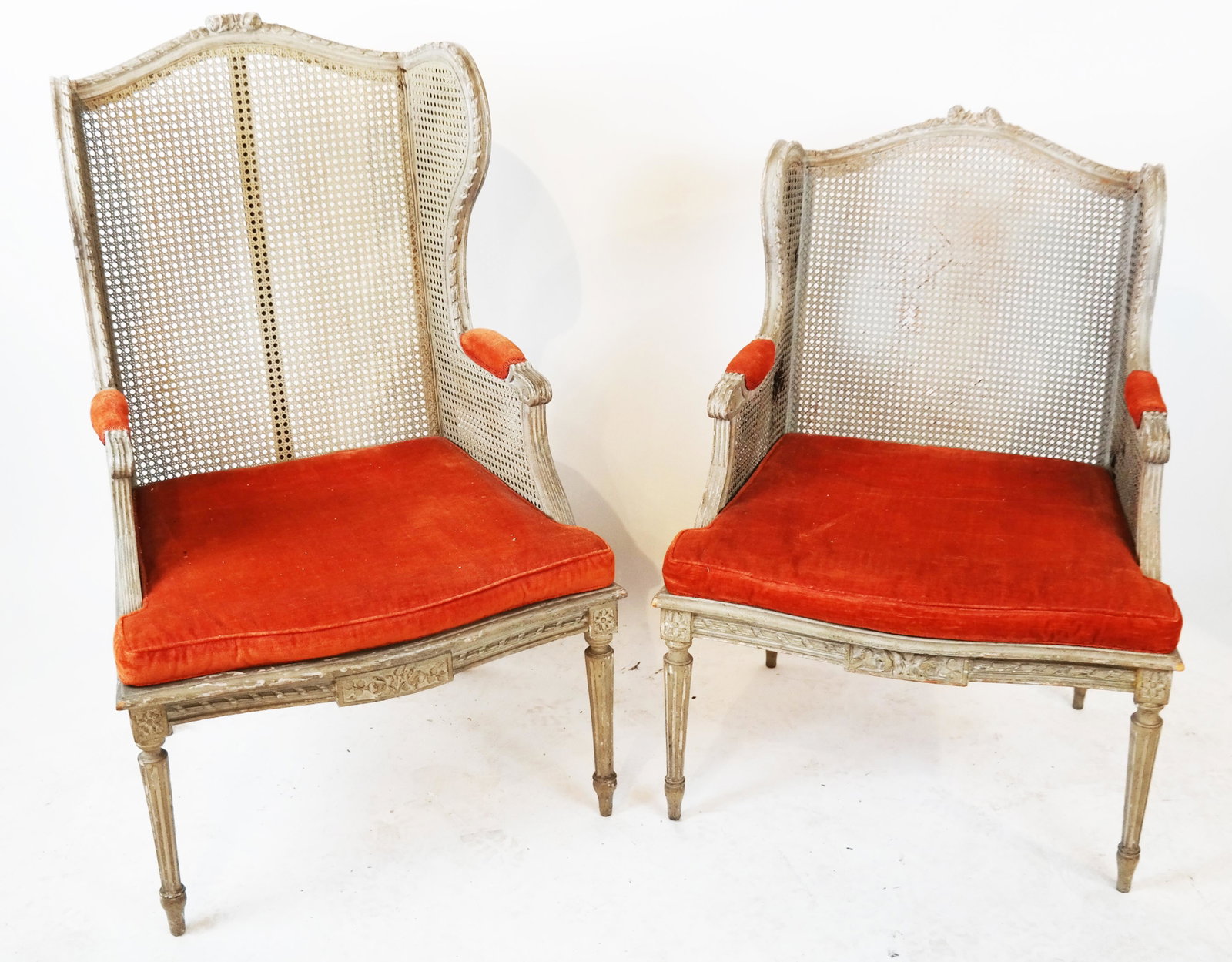 Pair of Matched French Bergeres: Pair of cream painted, caned bergeres, one larger than the other. [Larger: 56" HG x 26" W x 21" D]. Damaged cane.