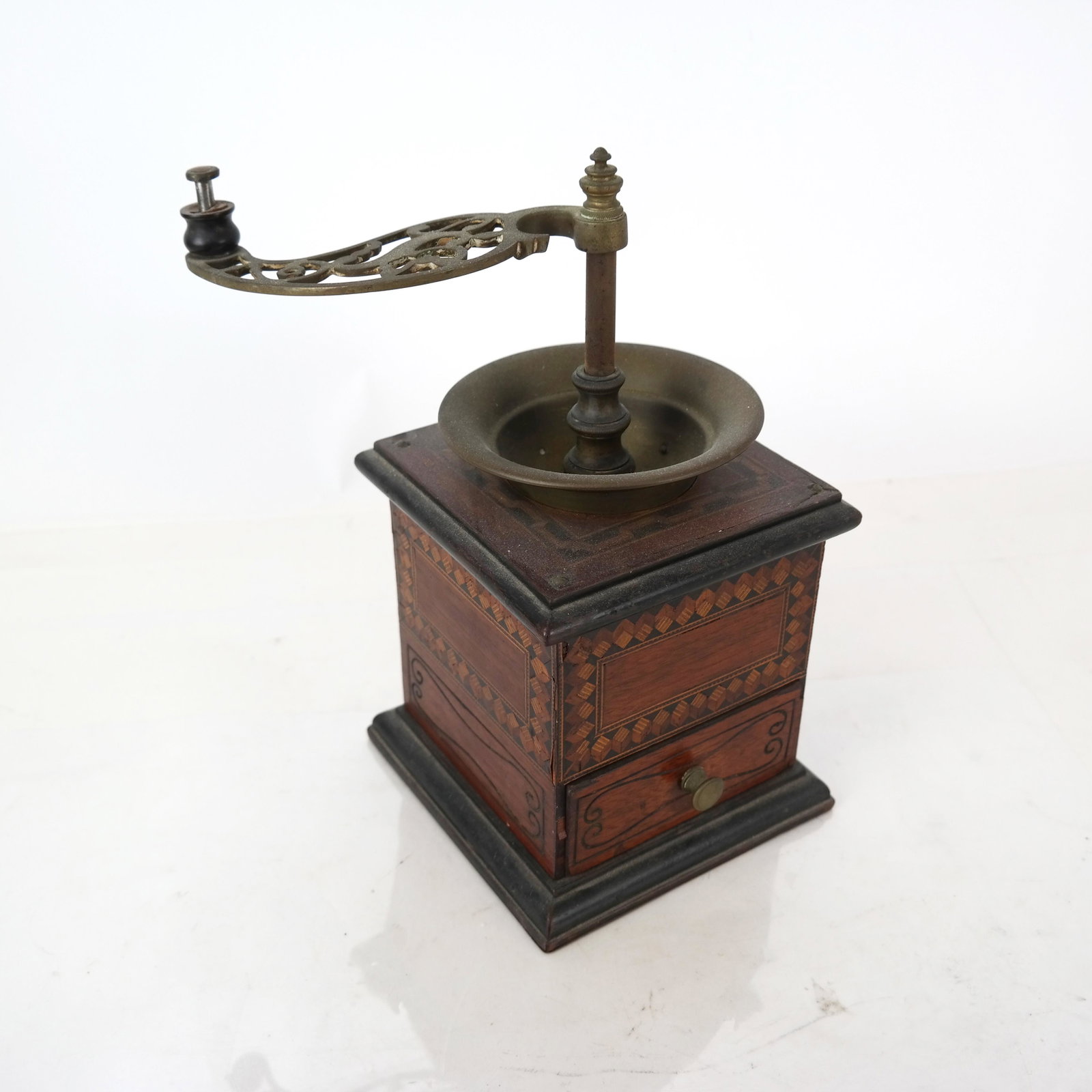 Folk Art Coffee Grinder: Folk Art coffee grinder, having a brass top with inlaid and incised wood body, with one drawer. [11" H x 6" W x 6" D; Handles: 6" H].