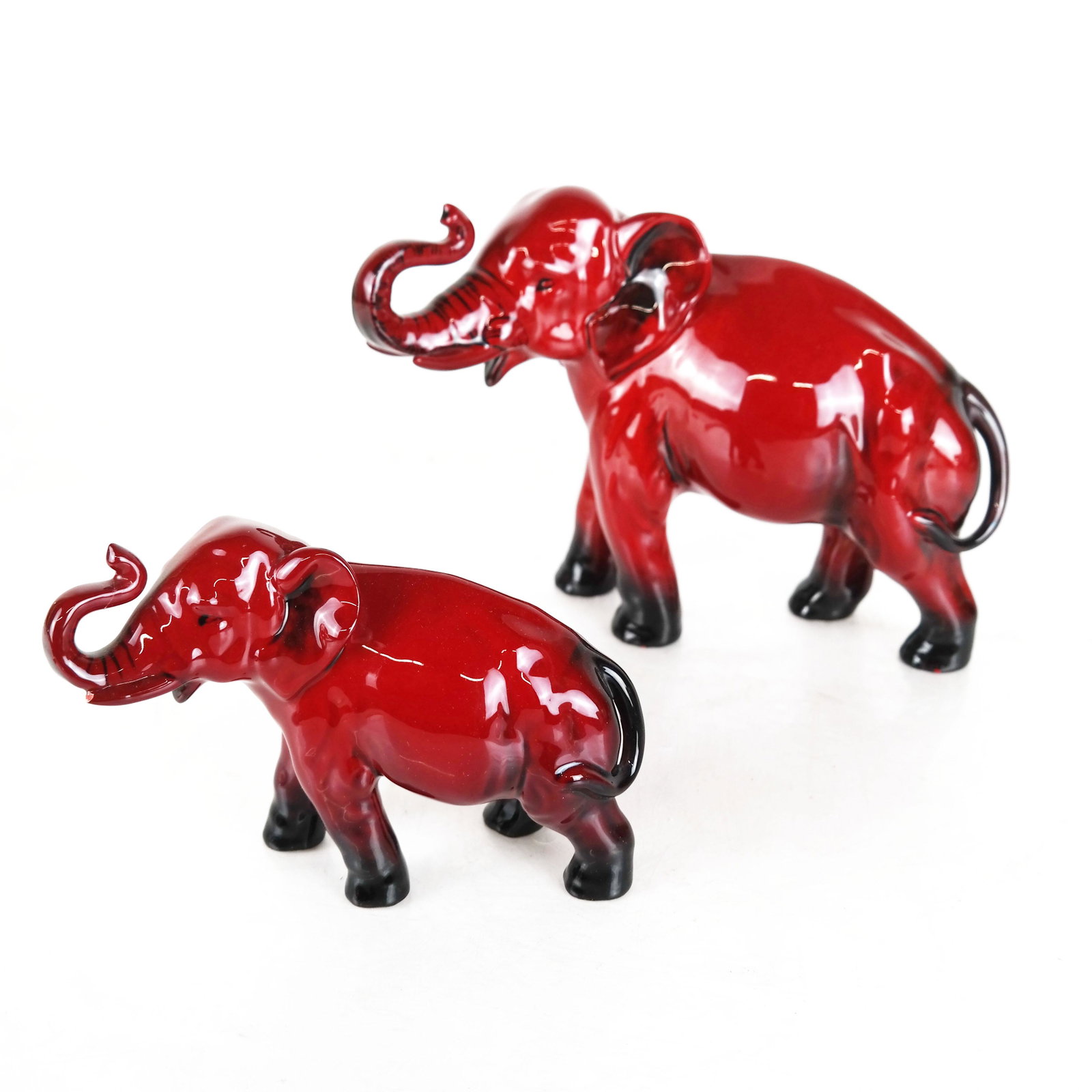 Two Royal Doulton Flambe Elephants: Two flambe porcelain elephants, with trunks up. [Larger: 5 1/2"H]. Smaller elephant's trunk with chip.