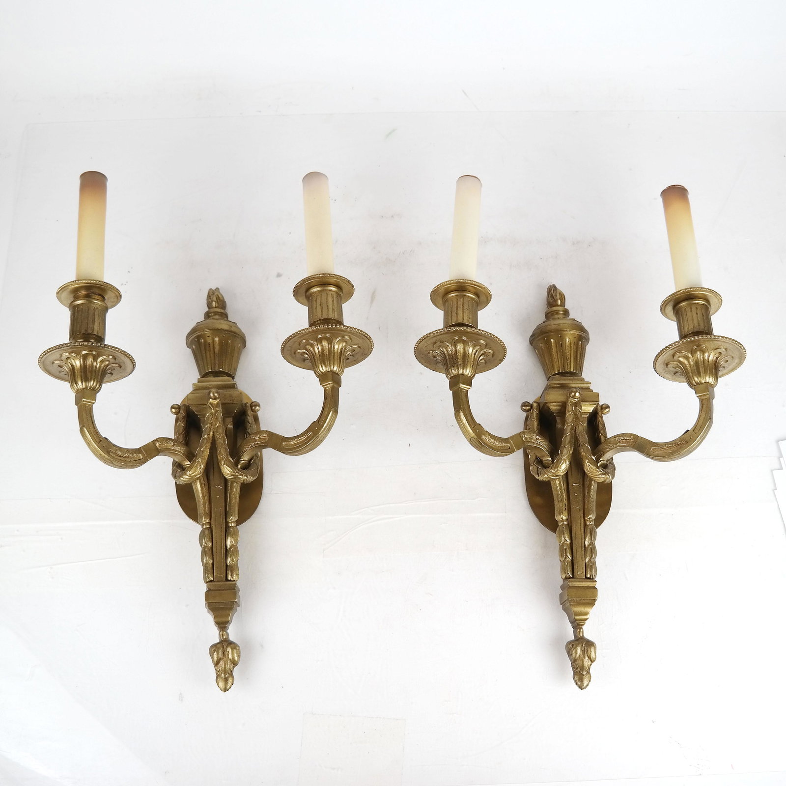Pair French-Style Bronze Sconces: Pair of French-style bronze sconces with two arms, having urn and valence backplates. [16" H x 10" W x 5" D]. In good condition.