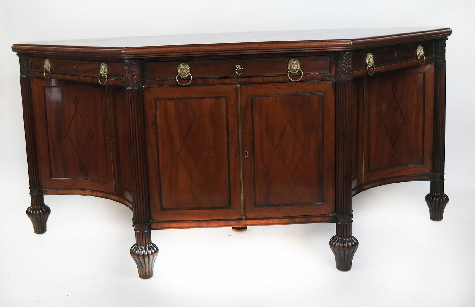 Pair of 19th C. English Regency Credenzas: Pair of early 19th century English trapezoidal shaped mahogany Regency credenzas, having capital and reeded columns ending in reeded bulbous legs; drawers over inlaid doors with side doors in curved c
