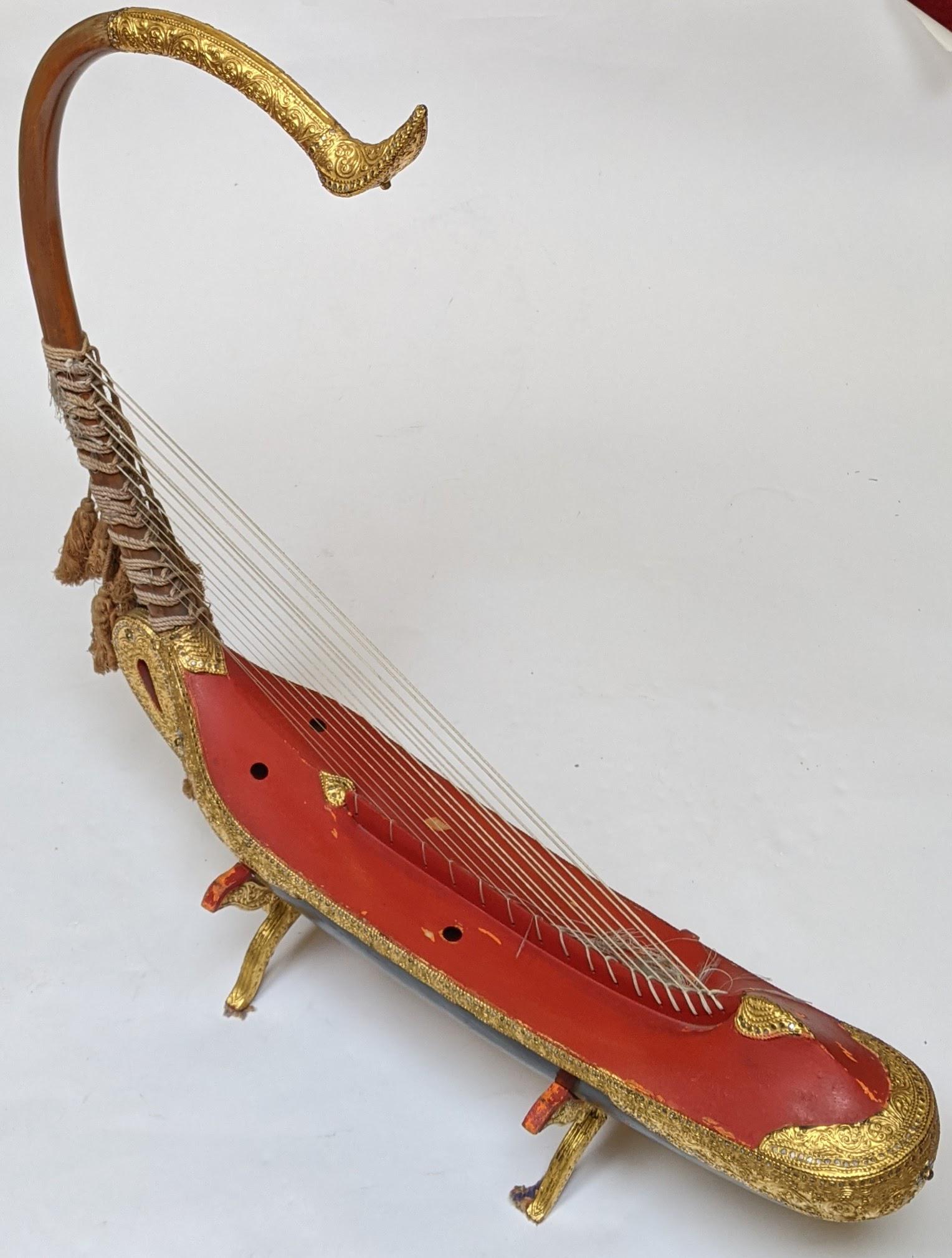Southeast Asian Boat-Form Harp: Boat-form harp on stand features gilt gesso accents with colored paste stones. [Overall: 33 1/2" H x 32 1/2" W x 6" D]. Light wear with some paint flaking and losses.