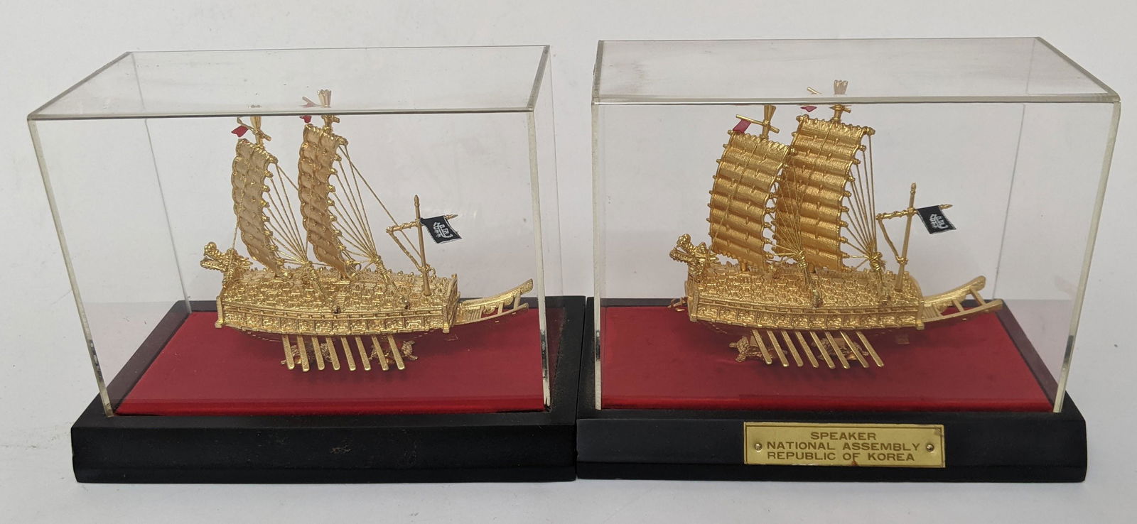 Pair of Chinese Brass 24K Plated Ships: Pair of Chinese 24K gold plated brass copies of armor-clad ships, under acrylic. [5" H x 6" W x 2 1/2" D]. In good condition.