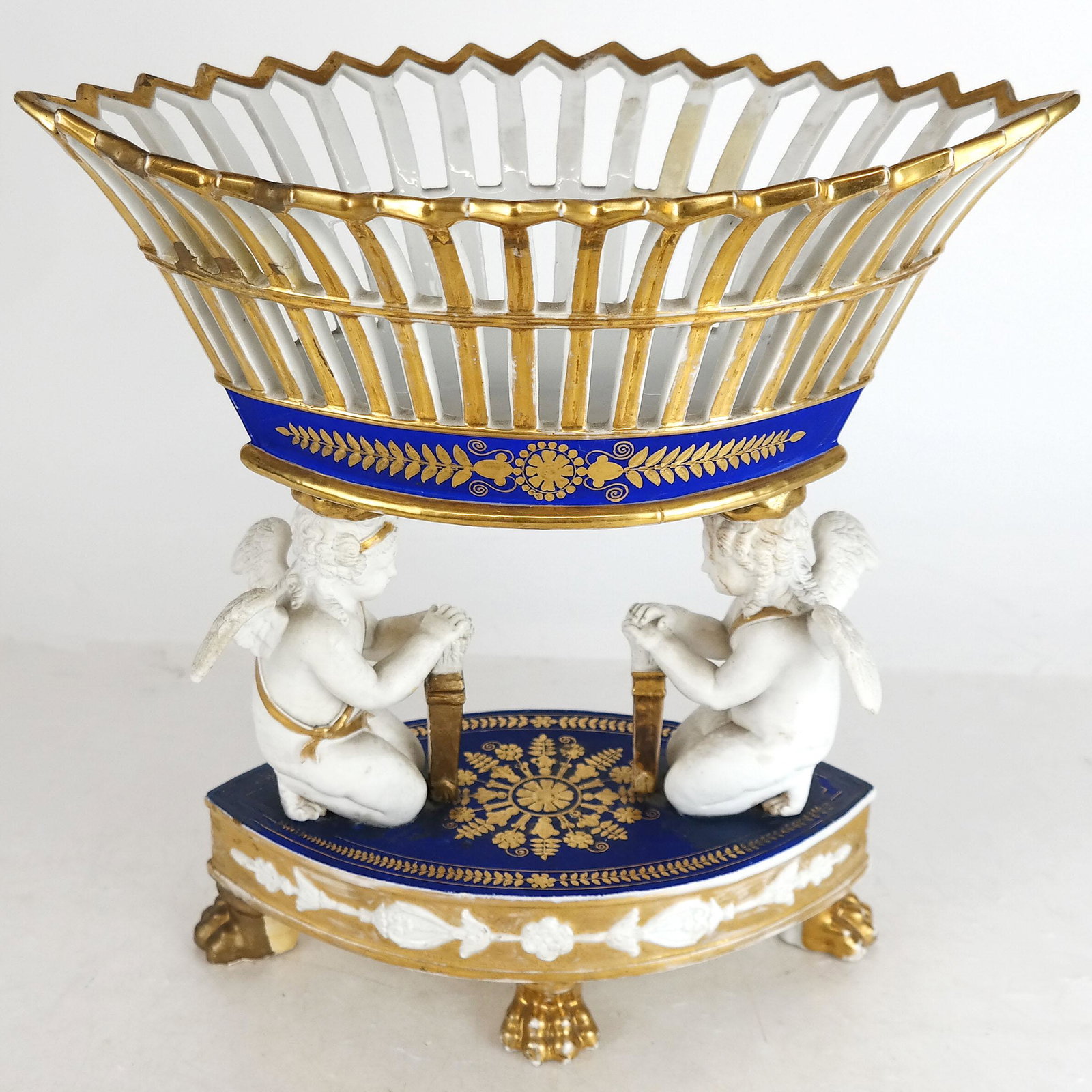 Paris Porcelain Reticulated Basket Centerpiece: Paris porcelain reticulated basket centerpiece, with cherub supports, on paw foot base. Not marked. [Overall: 12" H x 12" W x 6 1/2" D]. In good condition.