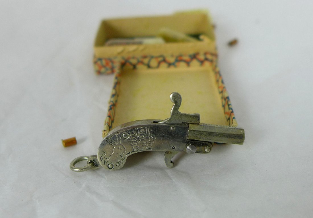 MINIATURE 2mm BERLOQUE PINFIRE PISTOL: Miniature cap gun fob in original box. A Miniature Berloque pinfire pistol, nickel plated with deer and rabbit design on grip. Marked made in Ausria. Works and fires extremely loud.