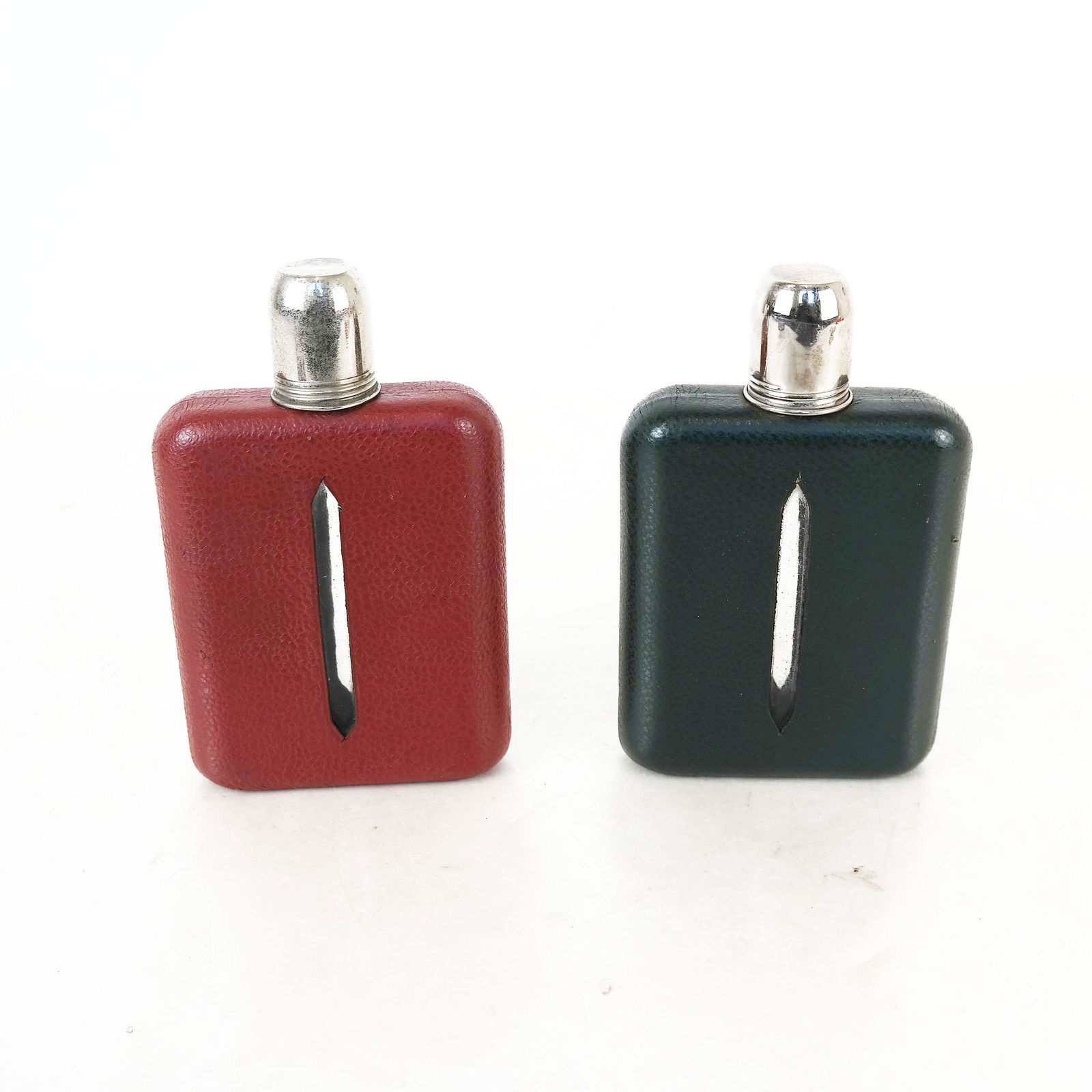 Two Leather Covered Hip Flasks: Two hip flasks having chrome double tops on glass, in red and green. [6" H x 4" W].