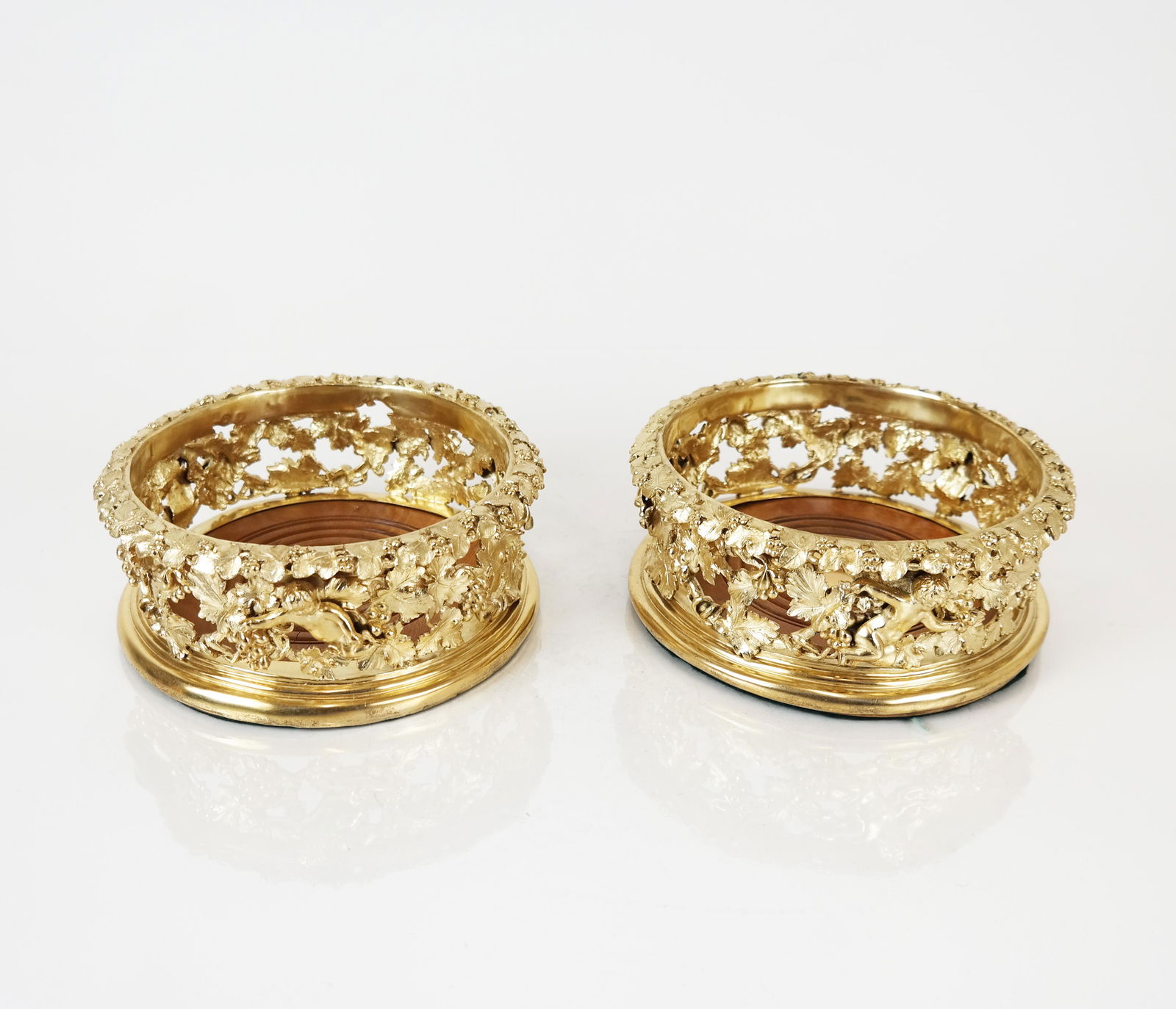 Pair of Gilt Wine Bottle Coasters: Pair of gilt wine bottle coasters, decorated with vine, grape cluster and Bacchanalian motifs. Possibly silver - marks not found. 49.38 ozt. inclusive. [3" H x 6 1/2" Diam.]