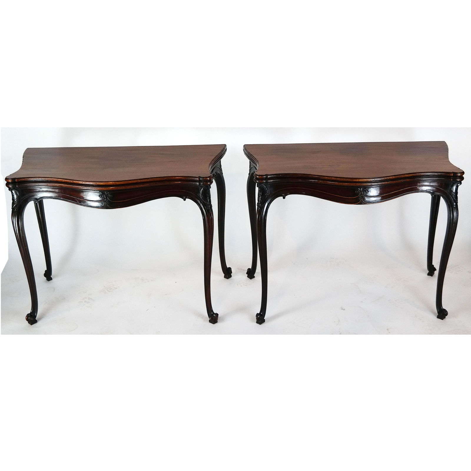 Pair of George III Mahogany Games Tables: A pair of George III carved mahogany serpentine fold-over tables, possibly Scottish, circa 1765, in the manner of Thomas Chippendale, having re-entrant corners, two-tier scrolled decoration to the fri