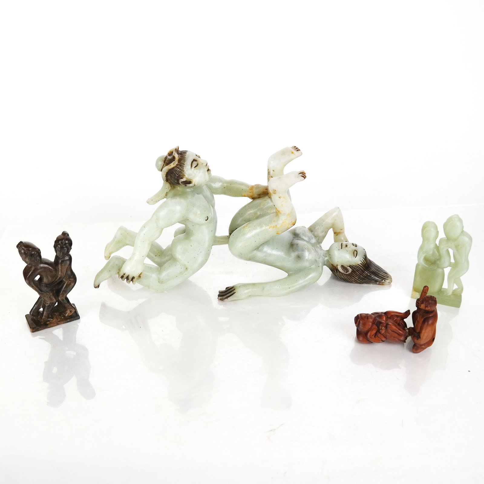 Group of Asian Erotic Carved Figurines: Group of Asian figurines of couples in erotic positions, variously carved from jade, hardstone and wood. Jade couple in bespoke fitted box. [Largest (jade couple): 5 1/2" H x 11 1/2" W x 3 1/2" D; Box