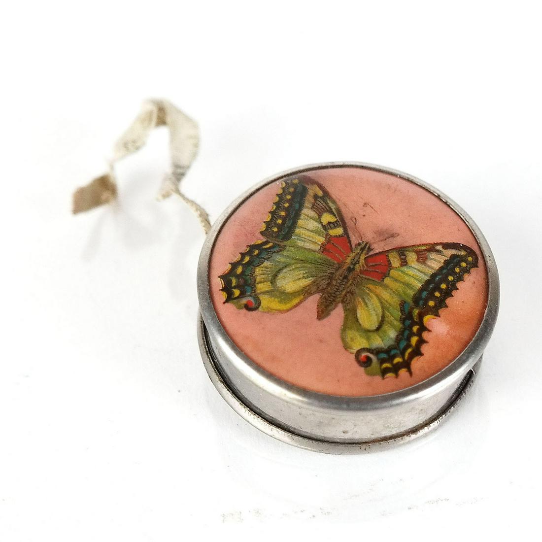Antique Cloth Tape Measure: Retractable cloth tape measure, in a metal case decorated with a butterfly painted porcelain plaque. [1 1/2" Diam.]. Allover wear; in working order.