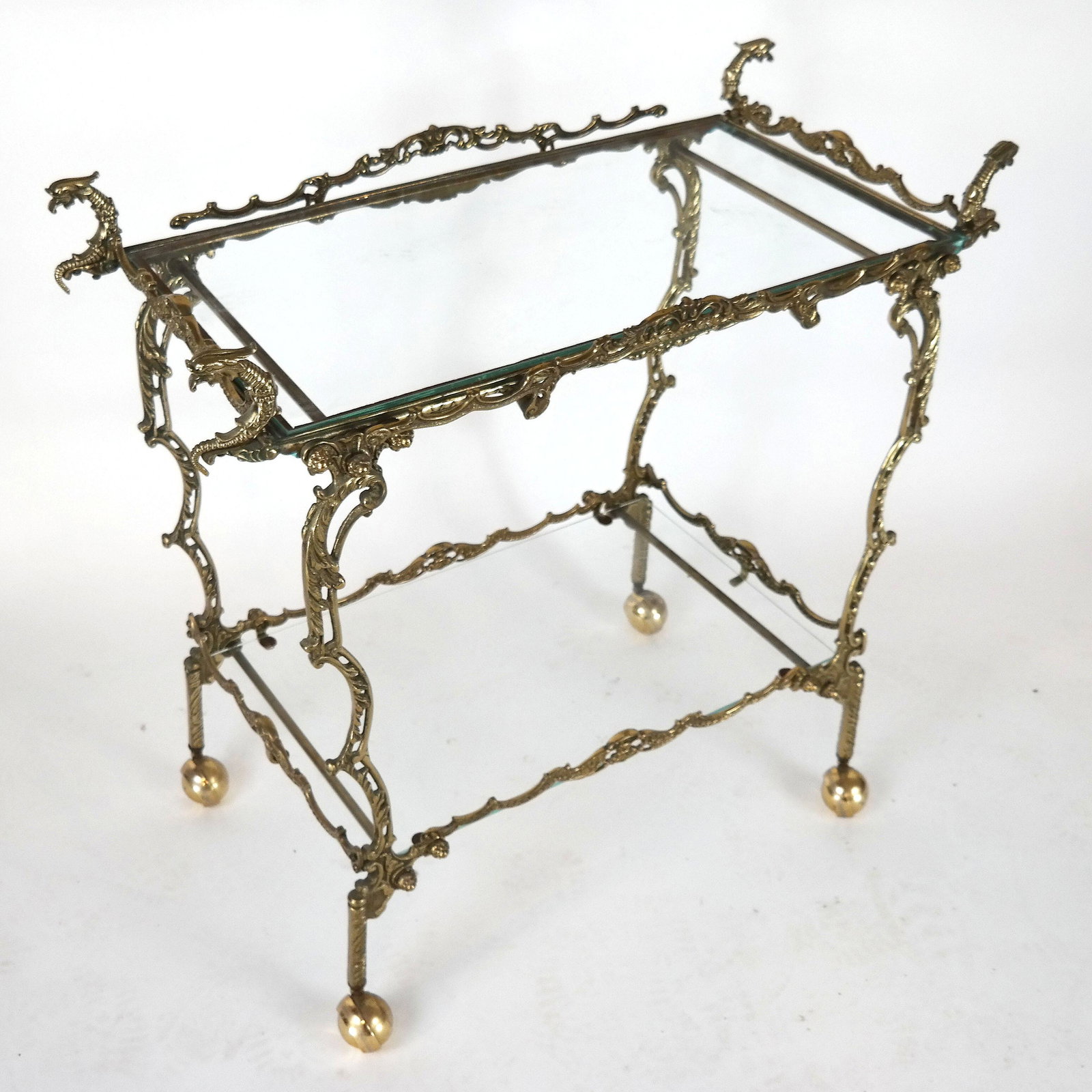 Two-Tier Gilt Metal Bar Cart: Two-tier gilt metal and glass bar cart, the terminals in the form of eagle's heads. [31" H x 32 1/2" W x 17" D]. In good condition.