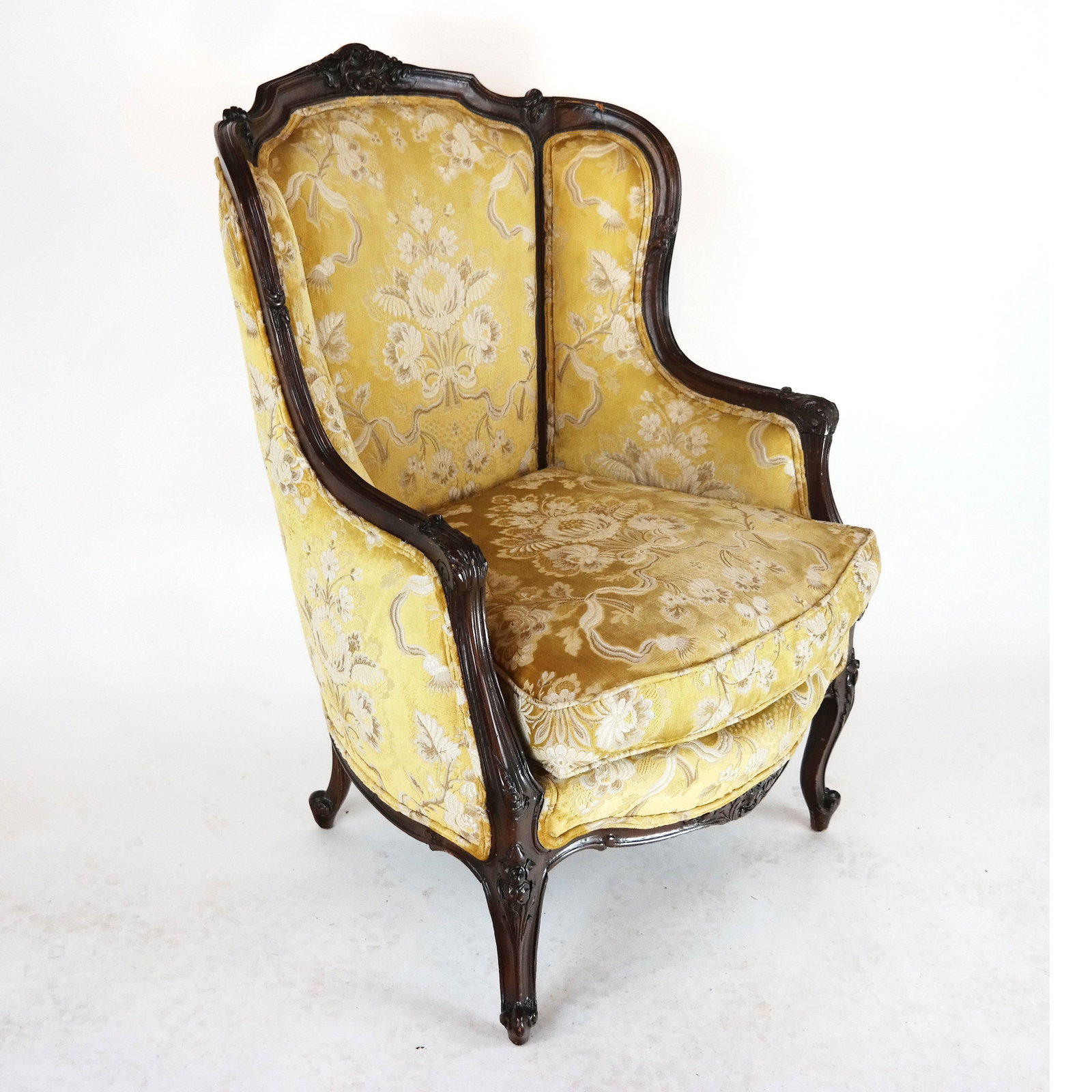 Louis XV-Style Gold Upholstered Wing Chair: 20th century French-style wing chair, with carved crest. [42 1/4" H x 28" W x 22" D]. In good condition as with age.