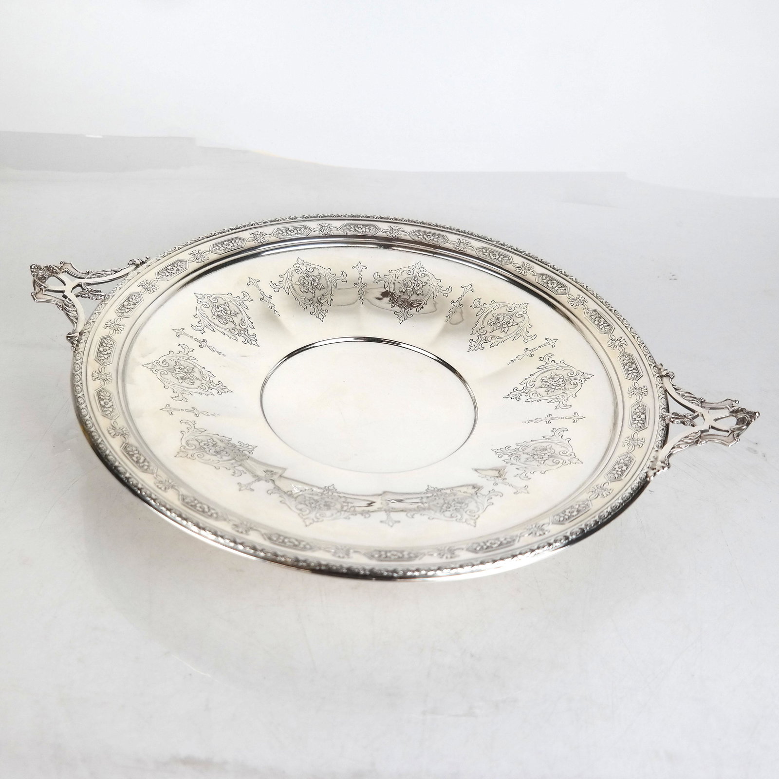 Sterling Silver Low Tazza: Neoclassical design low tazza with incised scrolling flora and two handles. 18.6 ozt. [3" H x 15" Diam. (including handles)]. In good condition.