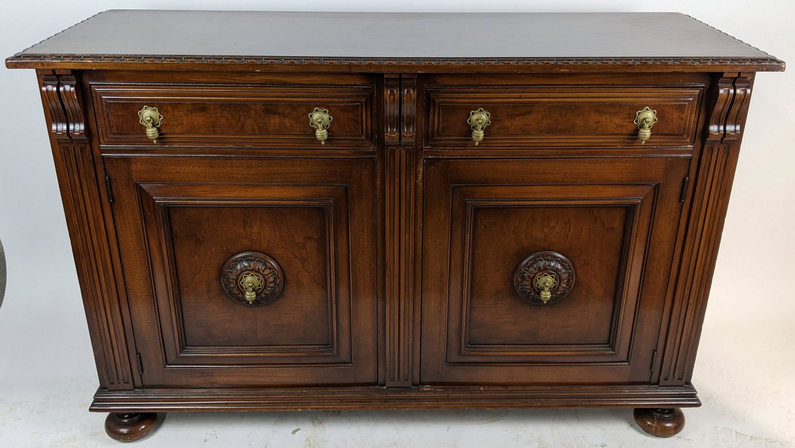 Walnut Carved Buffet: 20th century walnut two-drawer, two-door buffet, with carved and gadrooned top on bun feet. [37" H x 60" W x 21" D]. In good condition.