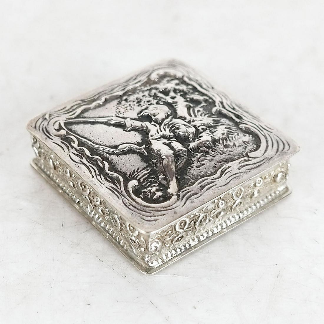 German Silver Pill Box: German silver pill box, having allover figural top design. Provenance: The Jay Waldmann Collection. 2.0 ozt. [1 3/4" H x 1 3/4" W x 1/2" D]. In good condition.