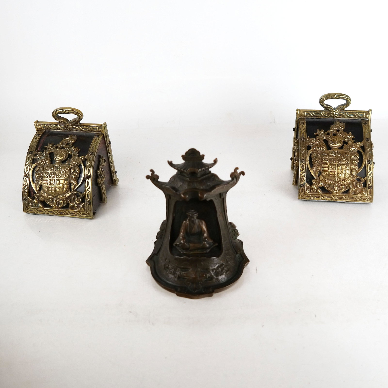 Three Bronze Bookends: A pair of coal bin-style bookends with coat of arms decoration. and a single Asian-style bookend with a seated Buddha. [ 5 1/2" H x 4 1/2" W x 4 1/4" D (x 2); [6" H x 5" W x 3 1/2" D (x 1)]. In good c