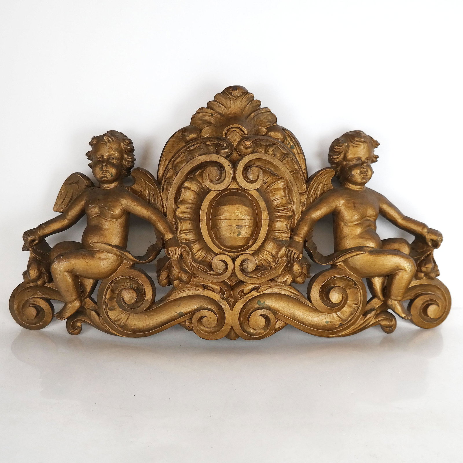 European Carved & Gilt Wood Baroque Cupid Crest: European carved and gilt wood Baroque cupid crest. [11 7/8" H x 21 3/4" W]. Age related wear with small repairs; shrinkage cracks; repainted.