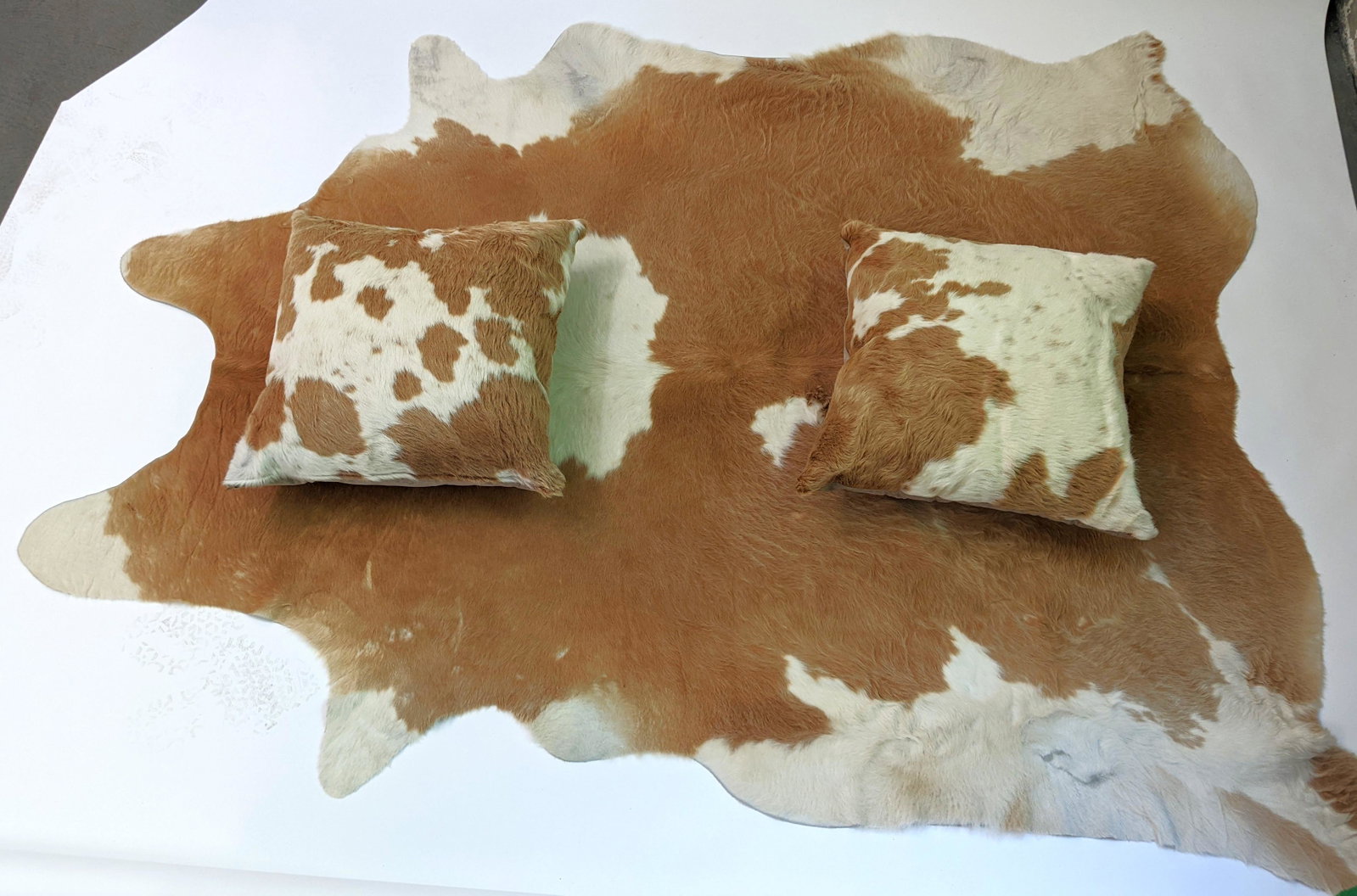 Pair Cowhide Pillows & Matching Rug: Rug with pair of matching cowhide pillows. From the Estate of June Hirsch Jones. [Rug: 91" x 67"; Pillows: 23" x 21"]. In good condition.
