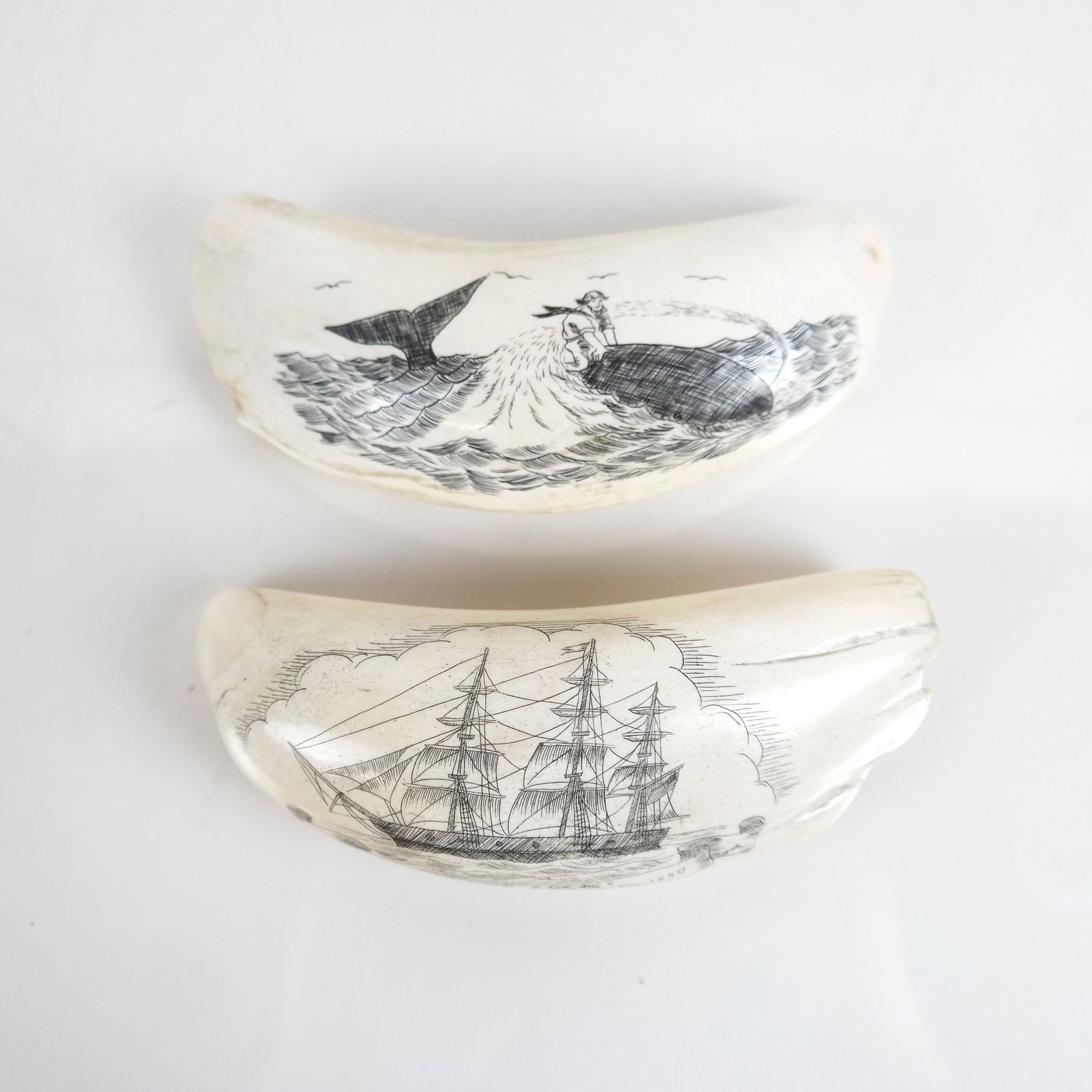 Two Antique American Engraved Scrimshaw Sculptures: Two scrimshaw sperm whale teeth, one inscribed "Game Cock," built by I. Hall, East Boston, 1850. Numbered 187 and 106 from a previous auction or collection. [5 1/2" Long].