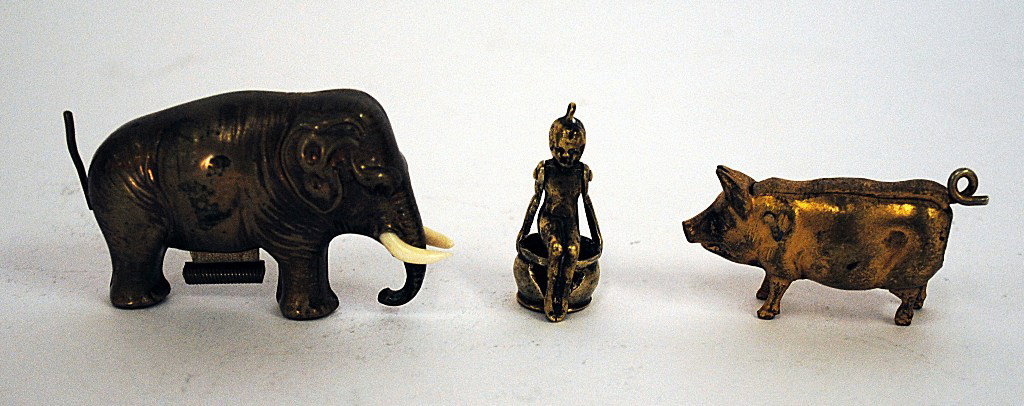 Tobacco: Group Of Three Mechanical Miniatures: Group of Three Miniature Mechanical Items. Comprises a brass elephant tape measure with two cigar cutters, one in the form of a pig, the other a woman on her chamber pot. Varying Dimensions: 1/2" to 3