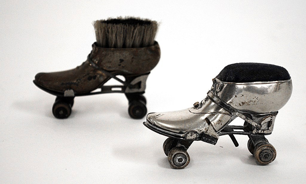 Two Miniature Roller Skate Items.: Two miniature roller skate items comprising a silver plate pin cushion and a brass pen wipe. Pin Cushion: 1"W x 2-3/4"D x 1-3/4"H. Pen Wipe: 3/4"W x 2-3/4"D x 2"H
