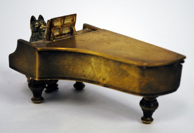 Whimsical Vienna Bronze Cat Pianist Match Safe: Vienna Bronze Match Safe depicting a cat seated at a grand piano playing sheet music. Top of piano is hinged and conceals the match reservoir and strike surface. 4-1/8"W x 1-7/8"D x 1-3/4"H.