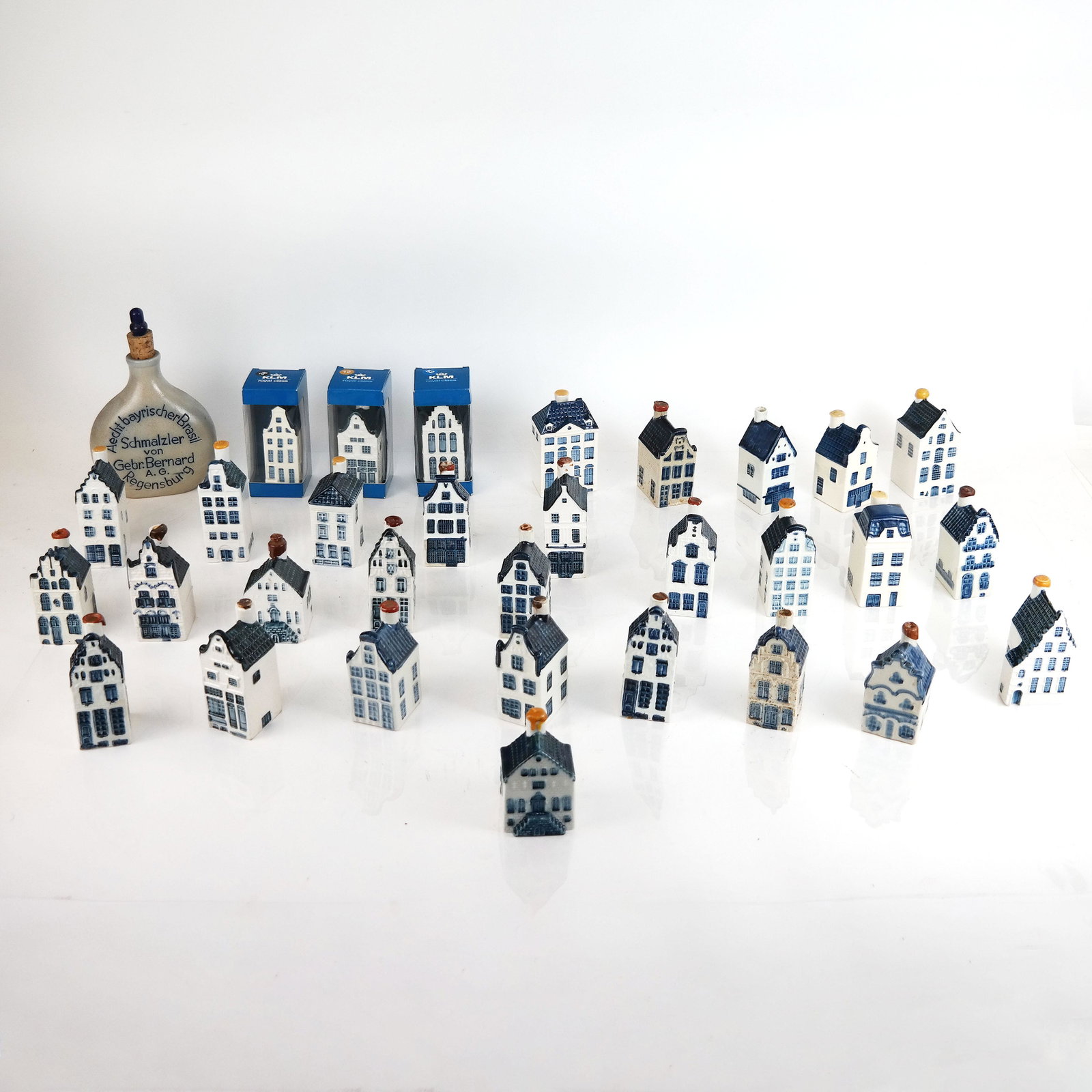 Group of Blue & White Miniature Houses: Group of 30 Dutch blue and white miniature houses, manufactured for KLM Airlines Business Class passengers, with marks, together with a larger bottle and wooden tray. [Large bottle: 8" H x 5 1/2" W x 