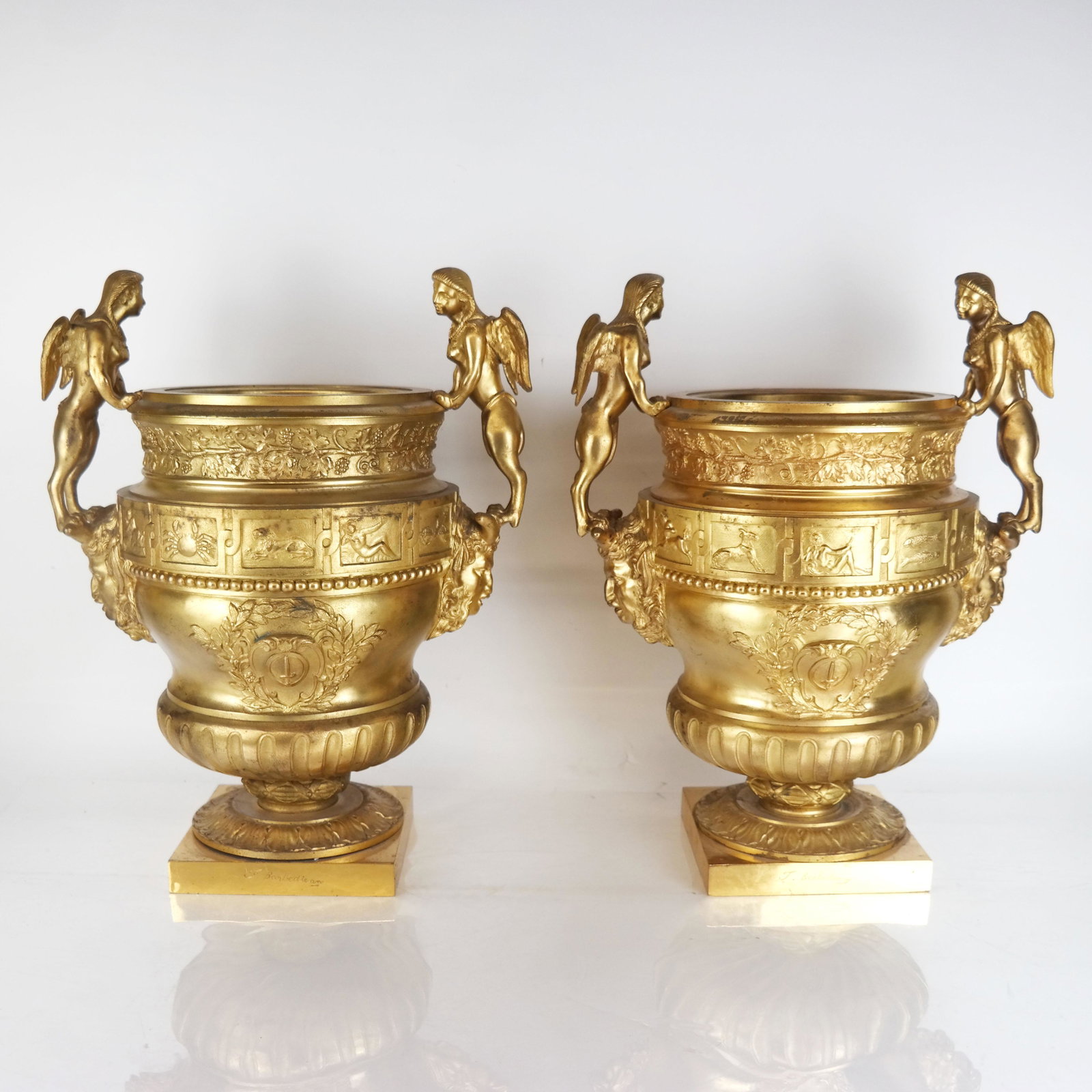 Pair Neoclassical-Style Gilt Bronze Wine Coolers: Pair of Neoclassical-style gilt bronze wine coolers, with winged figural handles over mascarons of Bacchus/Dionysus and grape leaf bands over astrological and allegorical cartouches, on associated pli