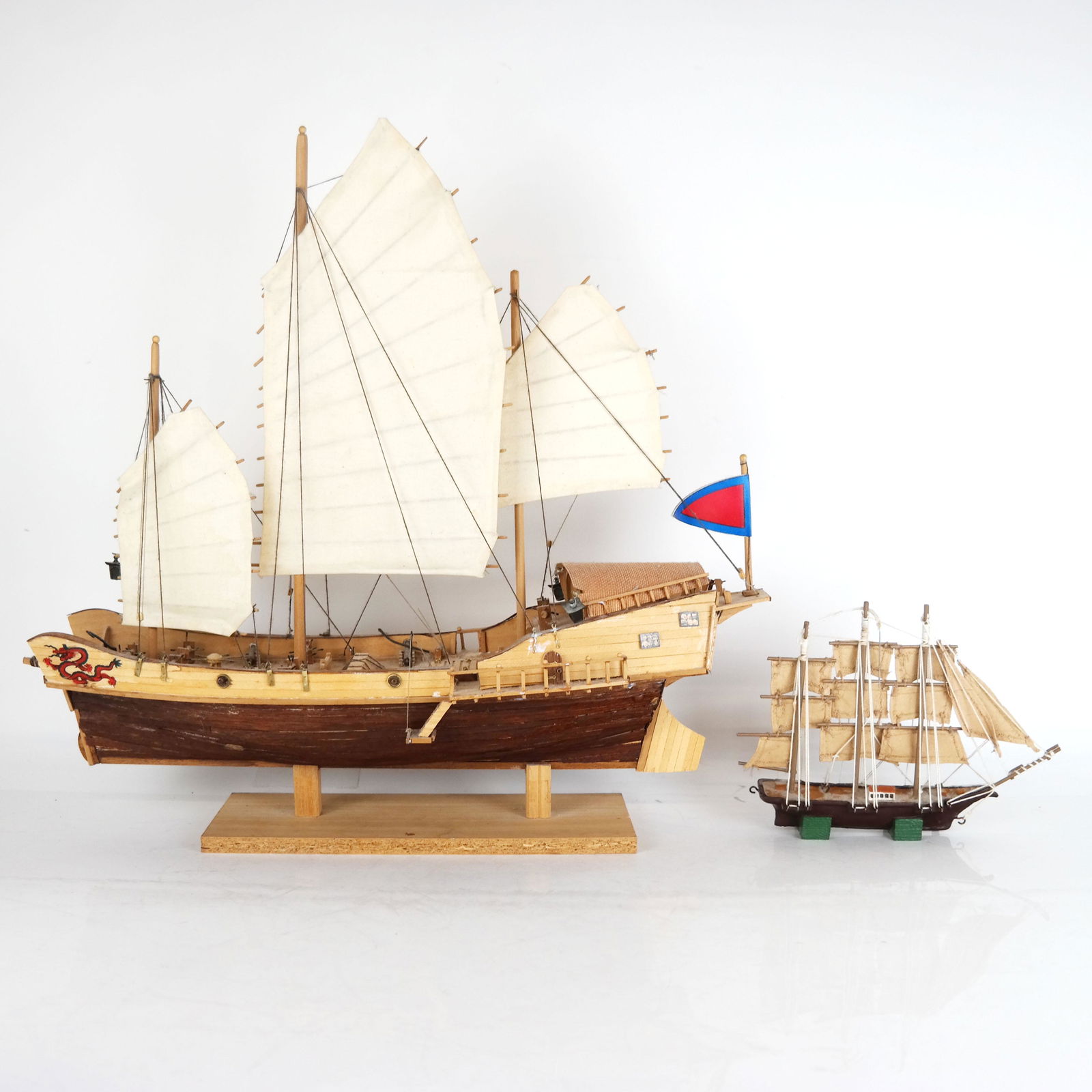 Two Ship Models: Two ship models, including one larger in the Chinese Junk form of wood and cloth with three sails [18" H x 19" W x 6" D], and one smaller of metal and cloth with three masts [6" H x 9" W x 2" D].