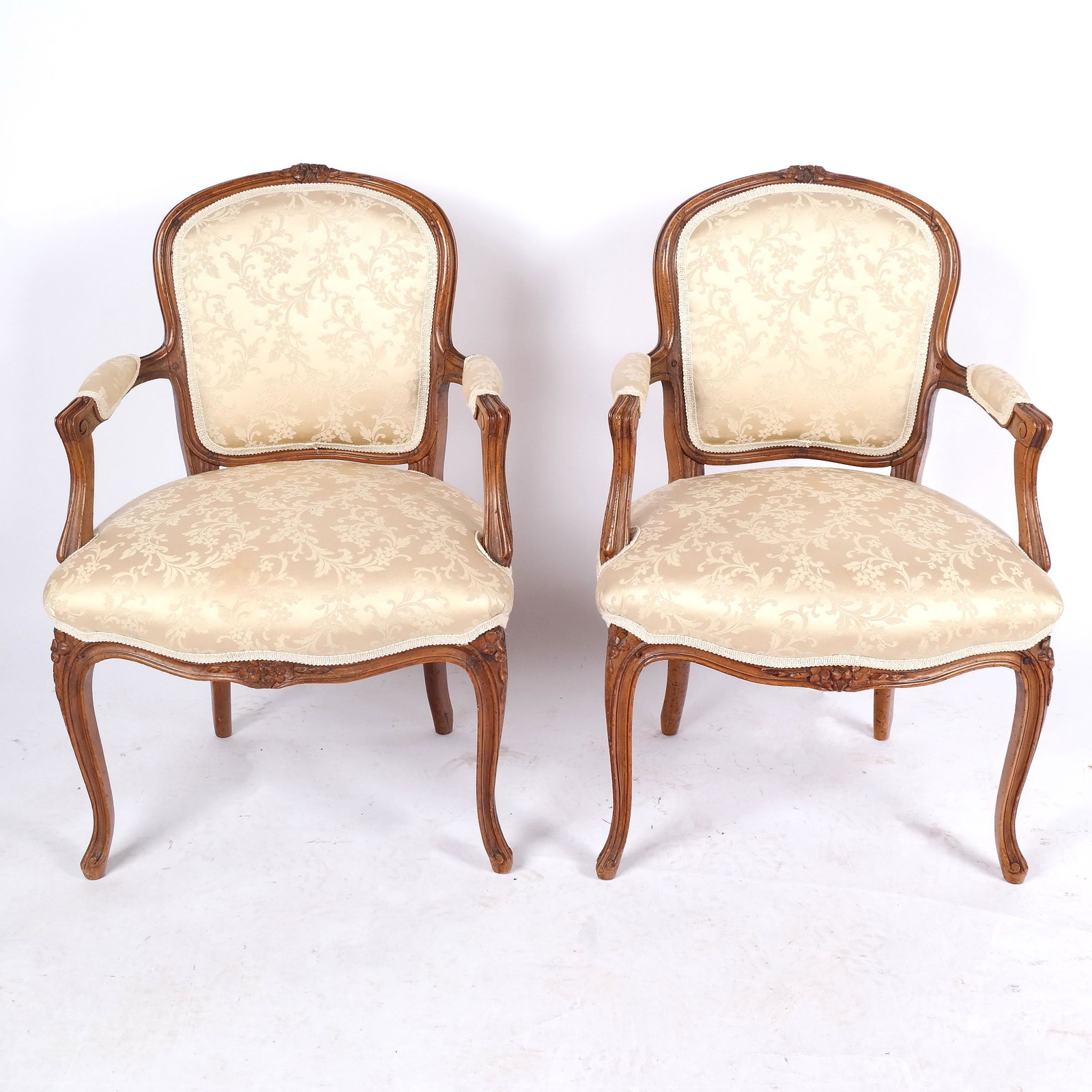 Pair of Louis XV-Style Carved Armchairs: Early 20th century pair of Louis VX-style armchairs, the fauteuils with scroll-motif upholstery. [33 1/2" H x 23" W x 22" D]. Some losses to carving, wear to frames and fabric.