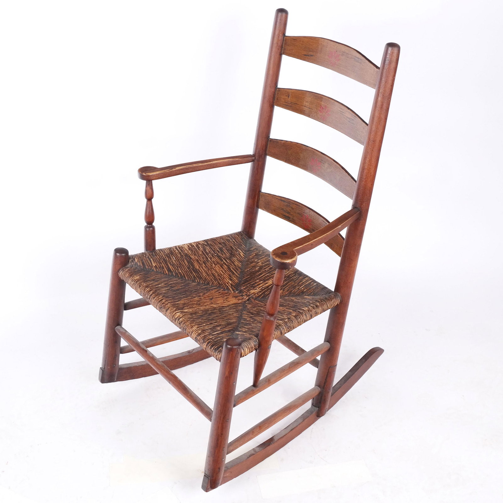 American Mixed Wood Rocking Chair: American mixed wood rocking chair, the back splats with red floral paint decoration over a rush seat. [36" H x 22 1/2" W x 26" D]. Stains, scuffs, marks, wear.