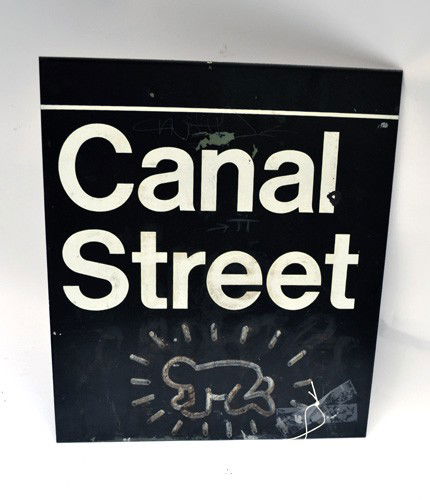 Keith Haring Canal Street Scene: A black metal sign "Canal Street" with a logo, possibly Keith Haring or in the manner of. Worn condition. 12" x 13.5".