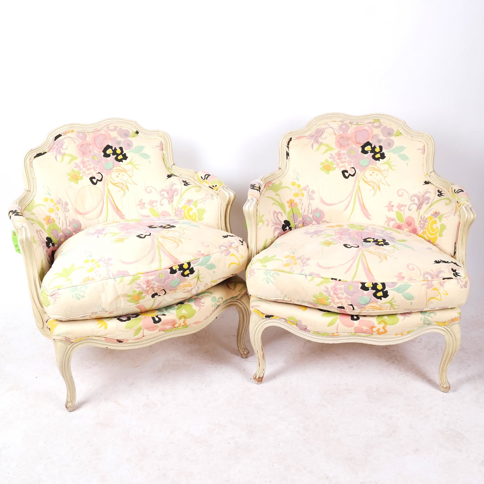 Pair of Louis XV-Style Bergeres: Pair of Louis XV-style bergeres, the armchairs with floral upholstery, circa 1940. [31 1/2" H x 26 1/2" W x 24 1/2" D]. Worn paint in some areas, showing signs of heavy use, upholstery soiled on both 