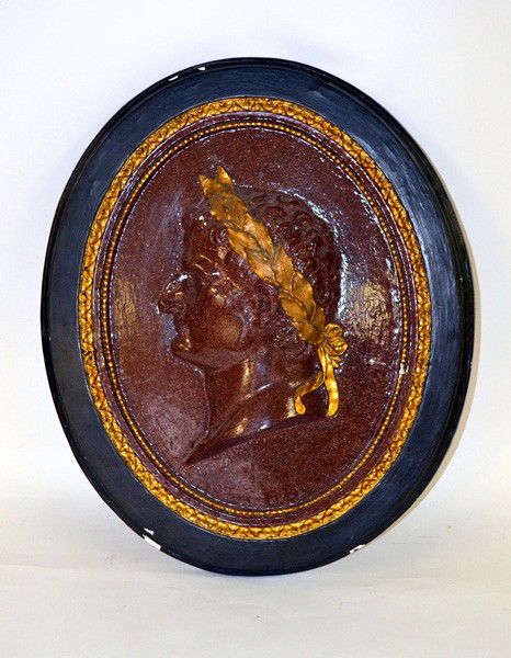Oval Raised Bust of Caesar in Ebonized Frame: An oval plaque with a raised bust of a Caesar profile in ceramic gilt redware speckle painted frame. Losses to ceramic. 21" x 18".