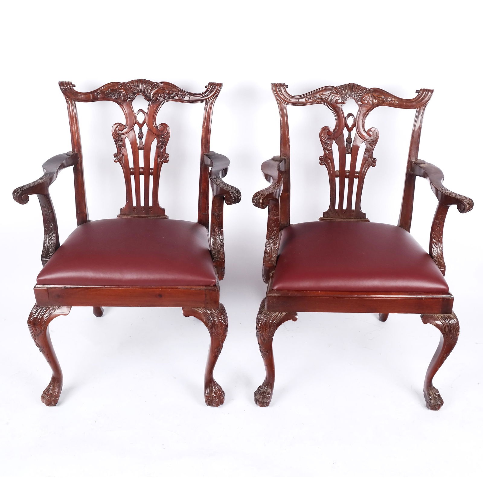 Pair of Chippendale-Style Mahogany Armchairs: Pair of Chippendale-style carved mahogany armchairs in the Georgian taste, with arched crest over tassel accented splats, curved arms around leather seats, raised on carved legs with hairy paw feet. [
