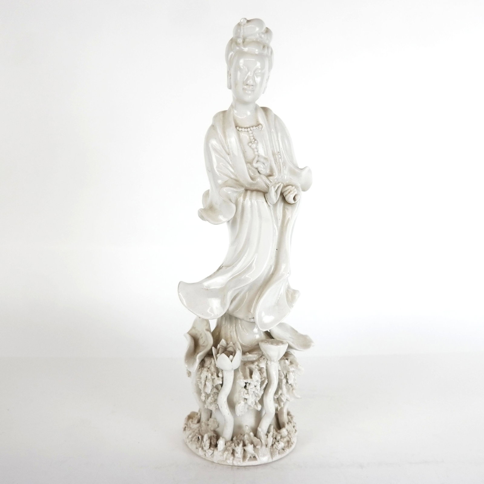 Chinese Blanc de Chine Porcelain Figure of Guanyin: Chinese Blanc de Chine porcelain figure of Guanyin, modeled as the Bodhisativa of compassion, mercy, and love, wearing a beaded necklace and billowing robe above lotus blossoms and leaves; partial lab
