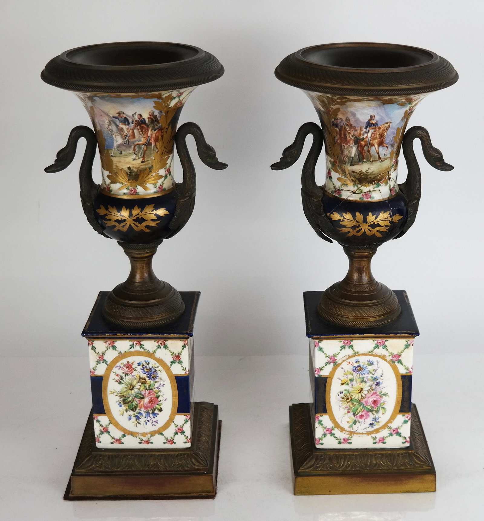 Pair of Neoclassical-Style Enameled Metal Urns: Pair of Neoclassical-style enameled metal urns of Campana-form with swan mounts, decorated with scenes of Napoleon and French officers on plinth bases. [14" H x 6" Diam.]. Breaks and restoration, wear