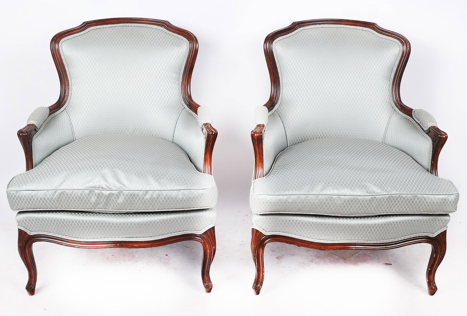 Pair of Louis XV-Style Upholstered Bergeres: Pair of Louis XV-style upholstered bergeres, the armchairs with carved details around upholstered panels. [35" H x 28 1/2" W x 29" D]. Minor wear to fabric, typical scuffs and marks to frame.