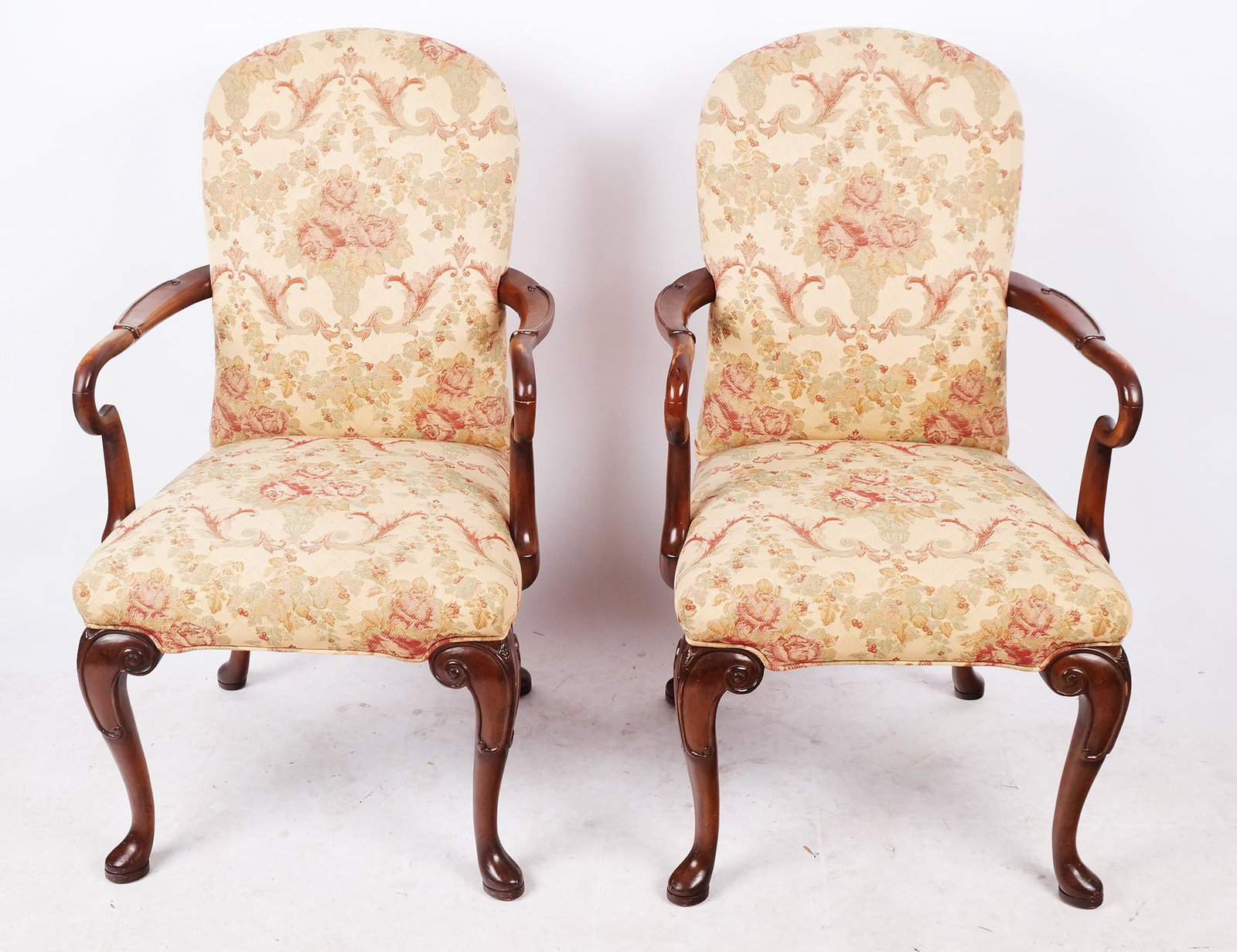 Pair of Georgian-Style Open Armchairs: Pair of Georgian-style open armchairs with floral upholstered seats between carved arms and legs with scrolling details, on pad feet. [42" H x 23" W x 24" D]. Wear to fabric, scuffs and losses to fini
