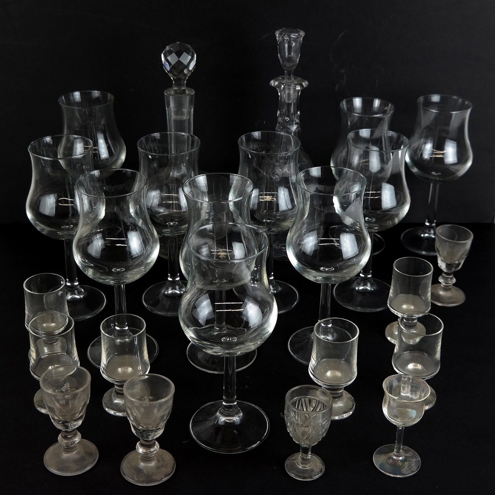 Assembled Group of Glass Barware: Assembled group of 22 pieces of glass barware, including 2 decanters, 11 wine goblets, and 9 cordial shot glasses; unmarked. [Tallest: 11 3/4" H x 4" Diam.]. Fleabite chips to stoppers, light residue 