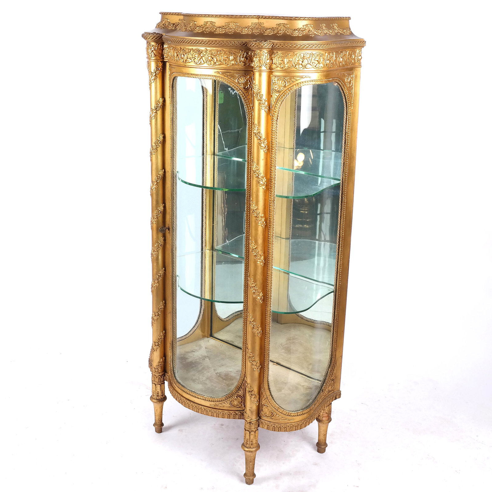 Rococo Revival Giltwood Vitrine Cabinet Circa 1900: Rococo Revival giltwood vitrine cabinet, with relief designs of festoons and foliate motifs to the case with curved glass panels; circa 1900. [57 1/2" H x 28 1/2" W x 16 1/4" D]. Some gesso appliques 