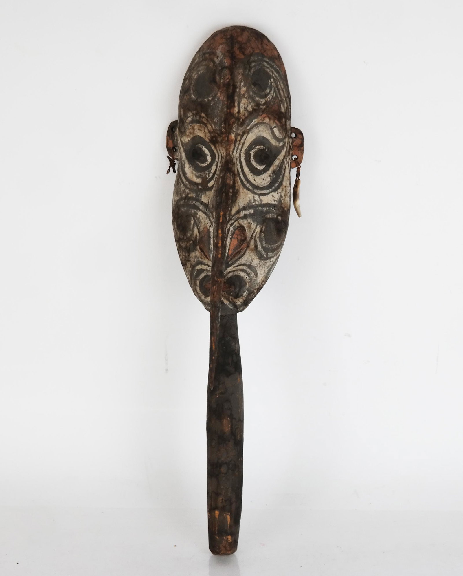 Small African Mask: Small African mask with handle, black and white design, pierced ears and nose. [17" H x 4 1/4" W x 2 1/2" D]. Water stains to wood.