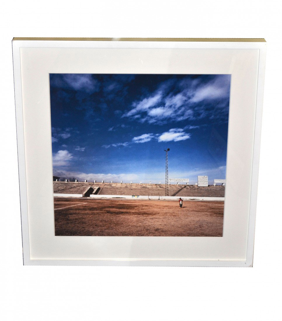 Harriet Logan Photograph: Photographic print depicting a young boy in a barren olympic playing field. Image: 19.5" x 19.5", Frame: 27" x 27". Signed on recto "Harriet Logan/Olympic stadium. Kabul 200 1/10". In excellent condit