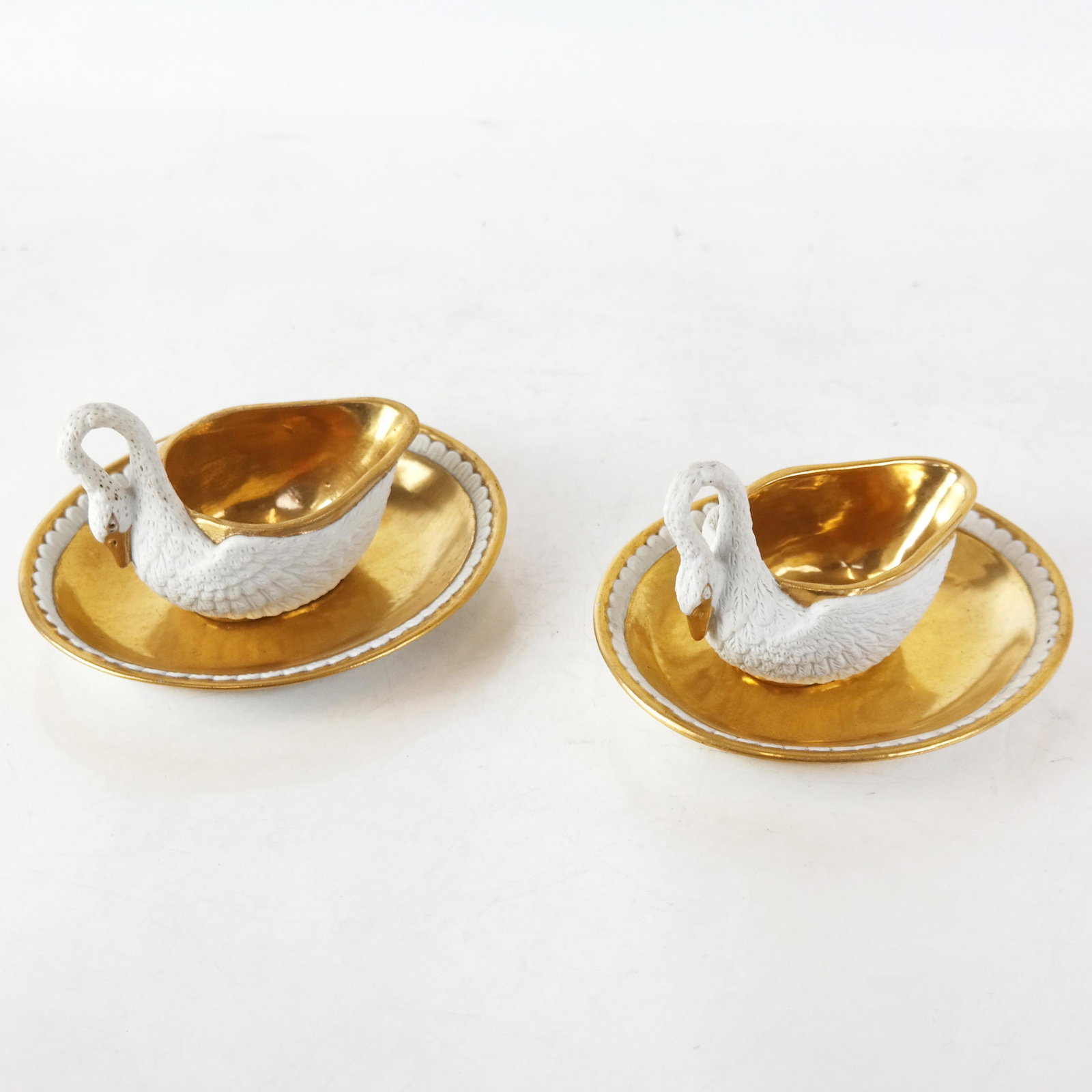Pair of Dagoty Paris Porcelain Cups & Saucers: Pair of 19th century Dagoty Paris French Imperial porcelain cups and saucers, possibly sauce/gravy boats, modeled as swans with gilt decoration and feather-motif border to saucers; marked to bases. [O