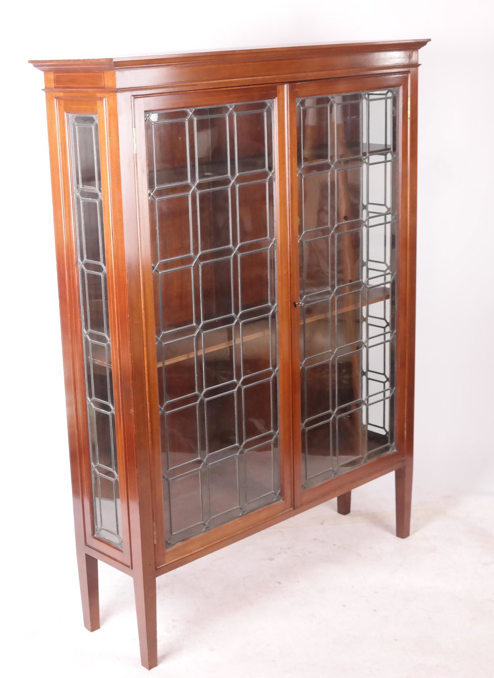 Leaded Glass Fronted Bookcase: Leaded glass fronted bookcase with twin doors, restrained inlay and traditional design. [64 x 48 x 14 inches]. In good condition.