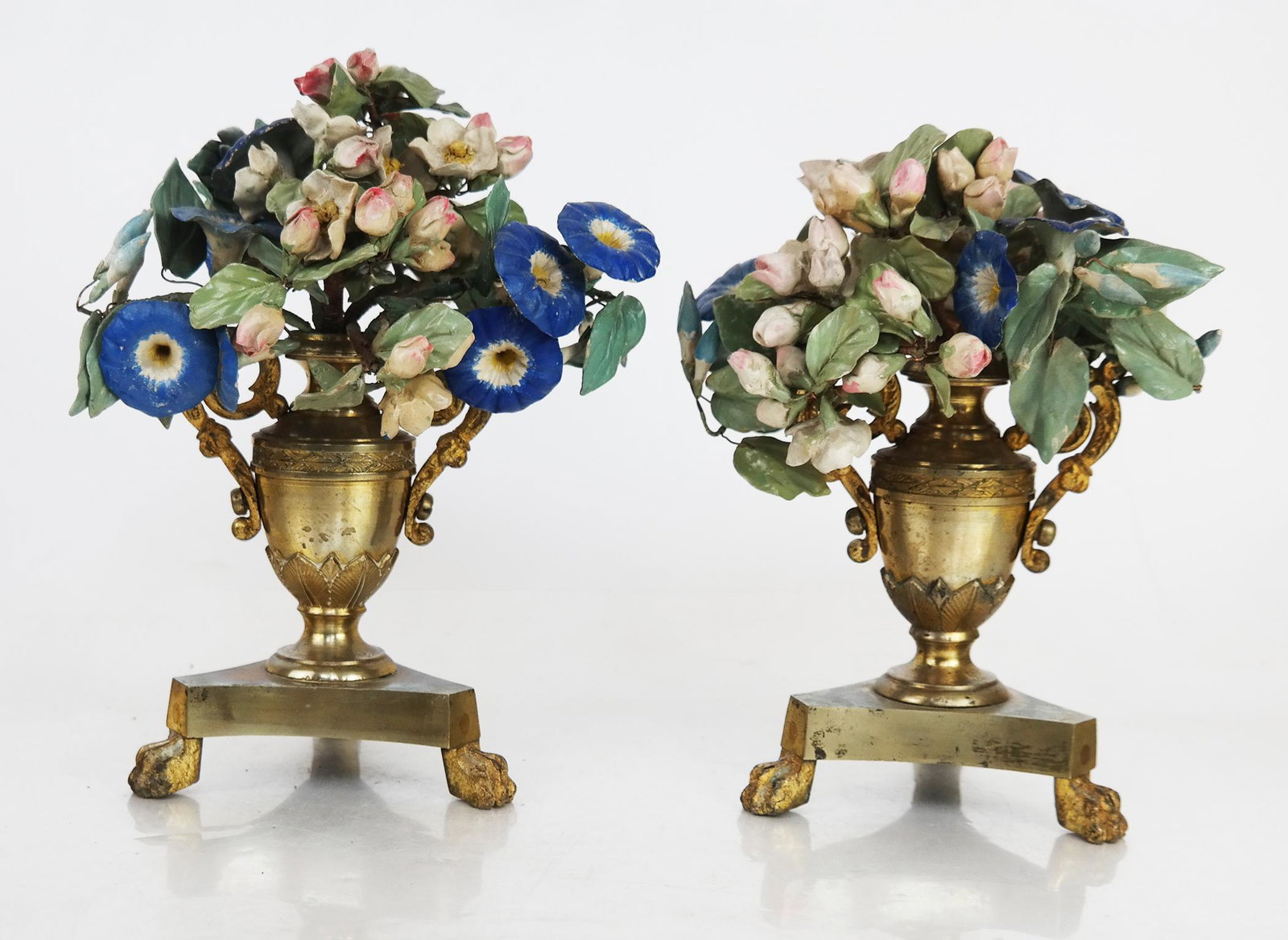 German Neoclassical-Style Floral Urns, Pair: Pair of German neoclassical-style floral urns with tole and porcelain flowers on a gilt metal urn-form base, with paw feet. [9" H x 7" Diam.]. Residue, losses and wear.