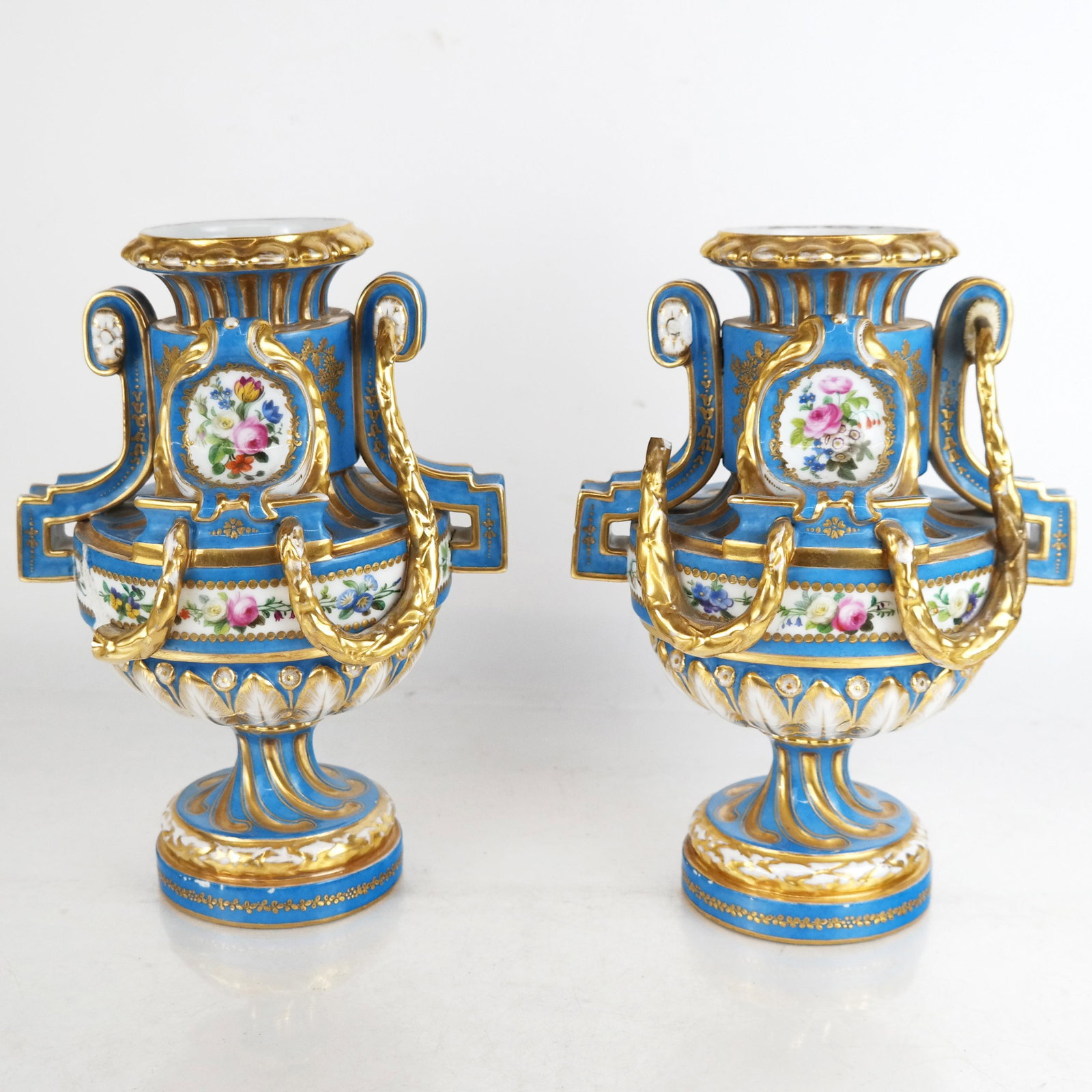 Pair of Louis XVI-Style Painted Porcelain Urns: Pair of Louis XVI-style painted porcelain urns, in the manner of Minton or Sevres with gilt and floral decoration on a blue ground; unmarked. [10 1/4" H x 7 1/2" Diam.]. Stress cracks around mount scr