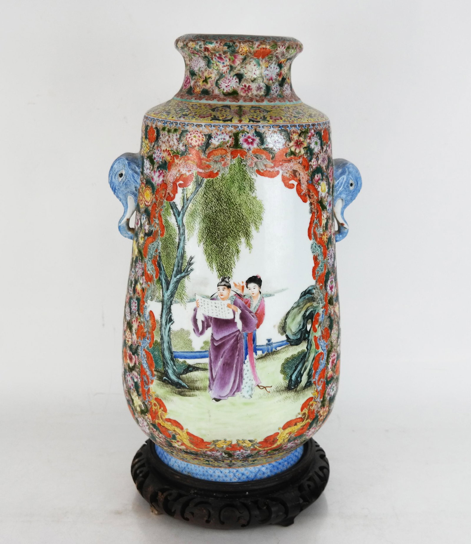 Chinese Porcelain Famille Jaune Medallion Vase: Chinese porcelain famille jaune medallion vase, with elephant handles flanking cartouches of figures in a garden; mark to base (drilled) on a carved wood stand. [Vase: 16 1/4" H x 9 1/4" Diam.]. Small