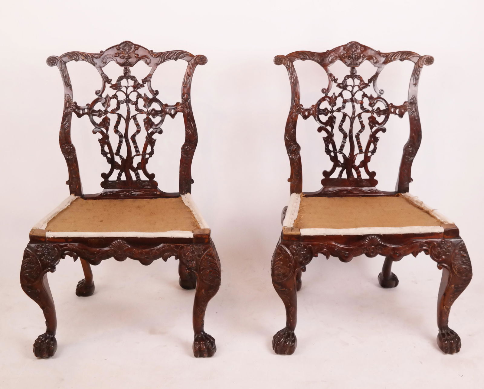 Pair of George III-Style Mahogany Side Chairs: Pair of George III-style chairs with exquisite ribbon backs, having all around carved rails, on hairy paw feet. Unupholstered seats. After a design by Thomas Chippendale. [39 x 24 x 20 inches].