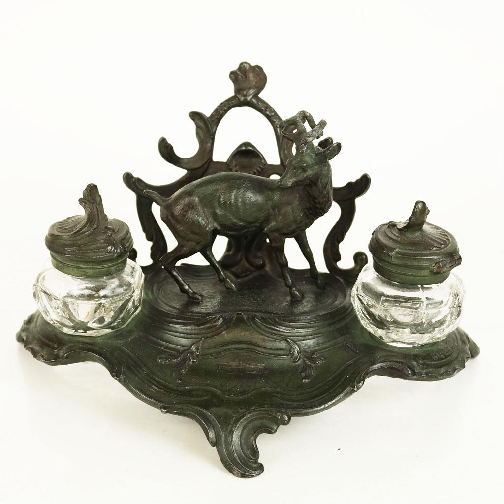 Rococo-Style Desk Stand Inkwell: Desk stand with inkwell modeled as a stag flanked by two glass ink pots. Late 20th century; unmarked. [6 1/4" H x 11" W x 7 1/4" D]. Marks and wear to applied patina; bending to antler.